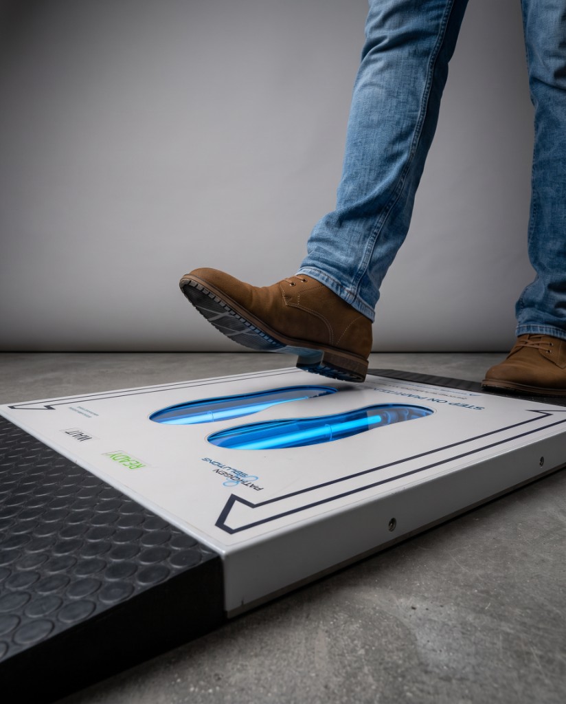 A facility worker stepping onto the UVZone® shoe-sole sanitizing station at an entry